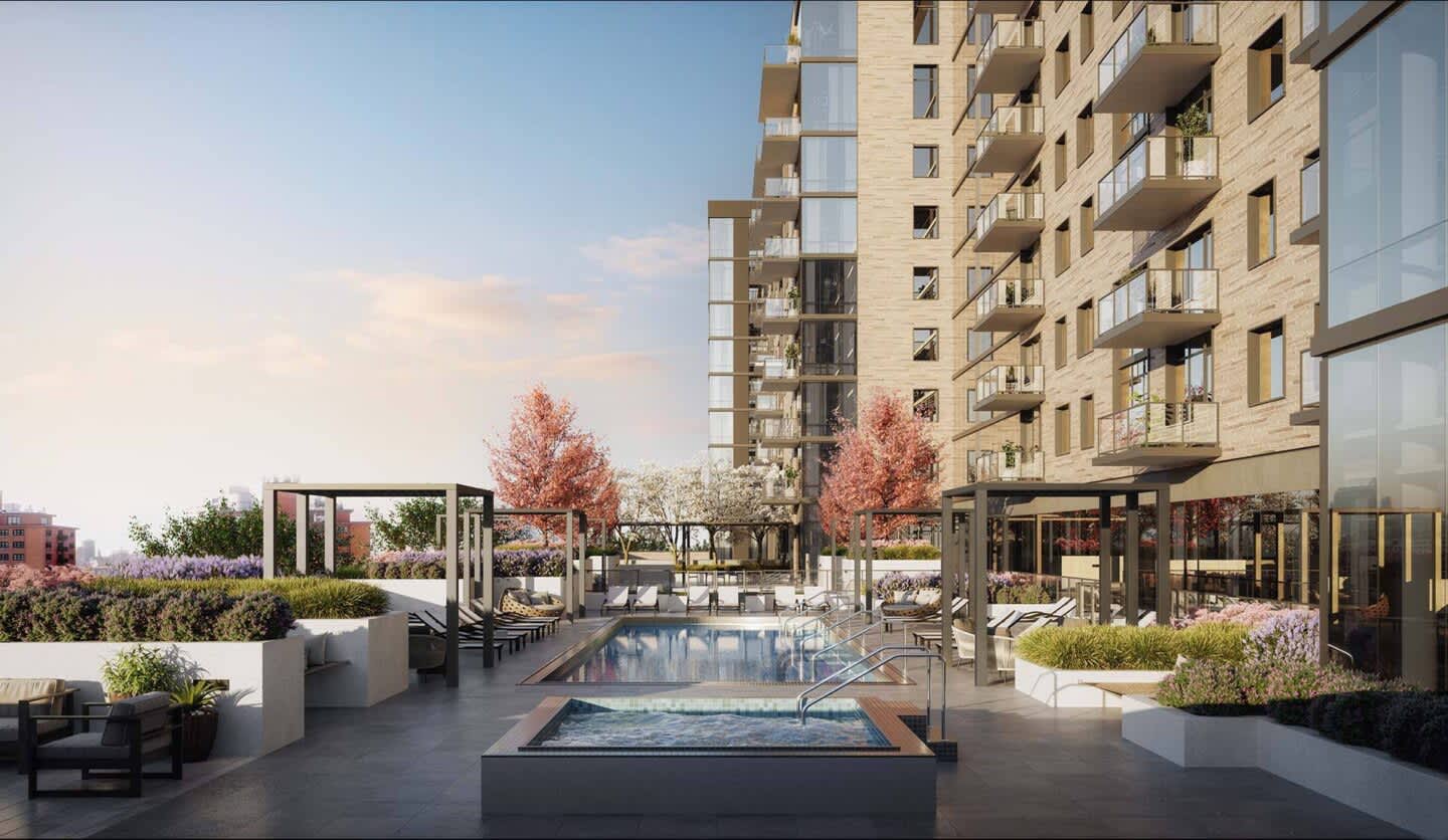 Rooftop pool and spa with lounge seating, pergolas, planters, and multi-story residential buildings in background under clear sky.