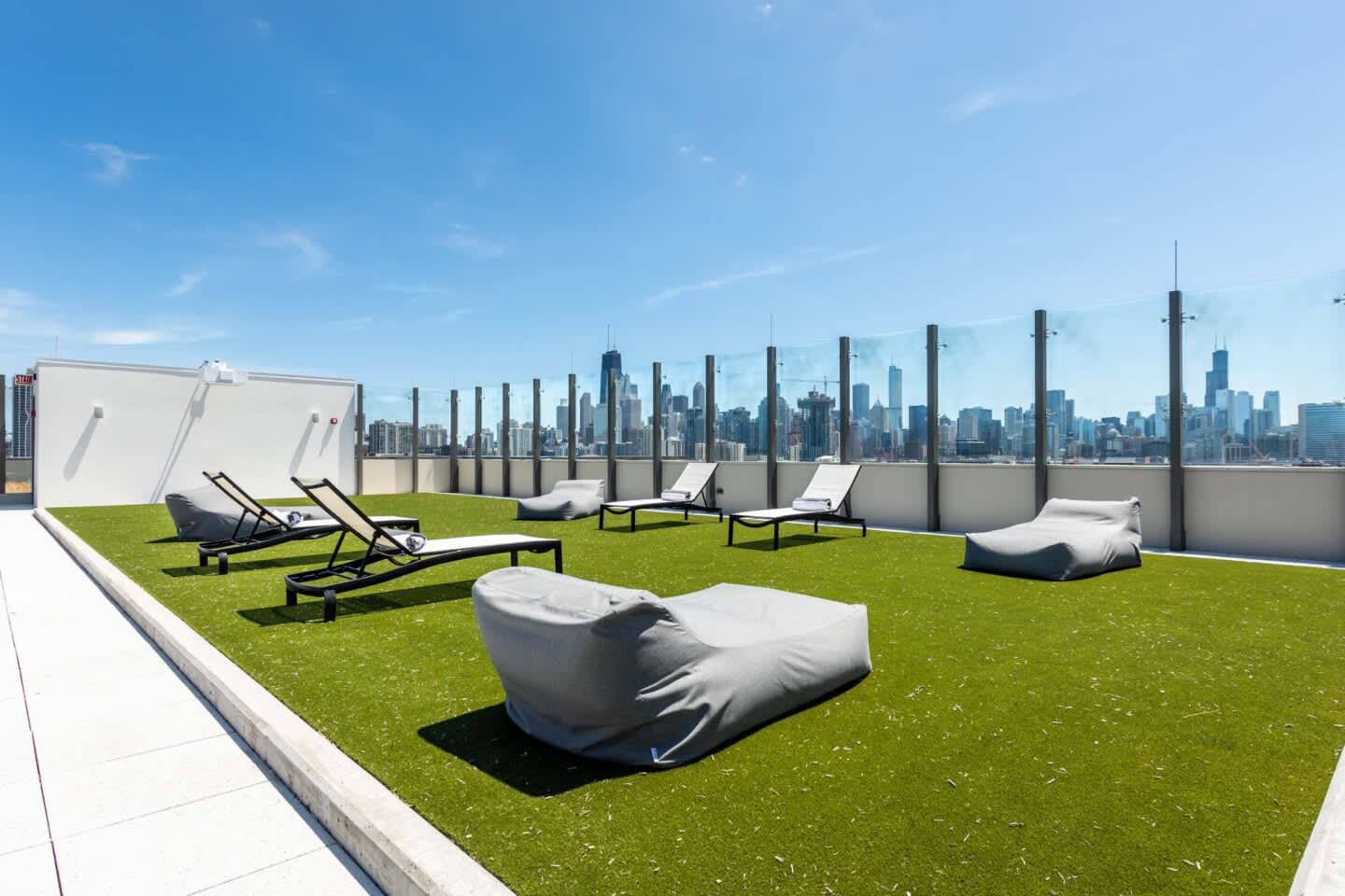 Rooftop terrace with artificial turf, lounge chairs, bean bag seating, and Chicago skyline view behind safety railing.