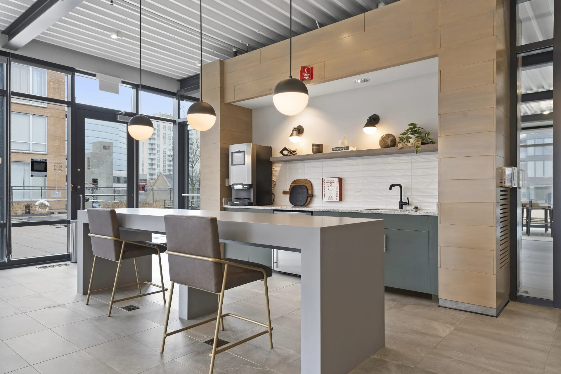 Contemporary kitchen with white waterfall island, two gray bar stools, pendant lights, wood cabinetry, and large windows with city views.