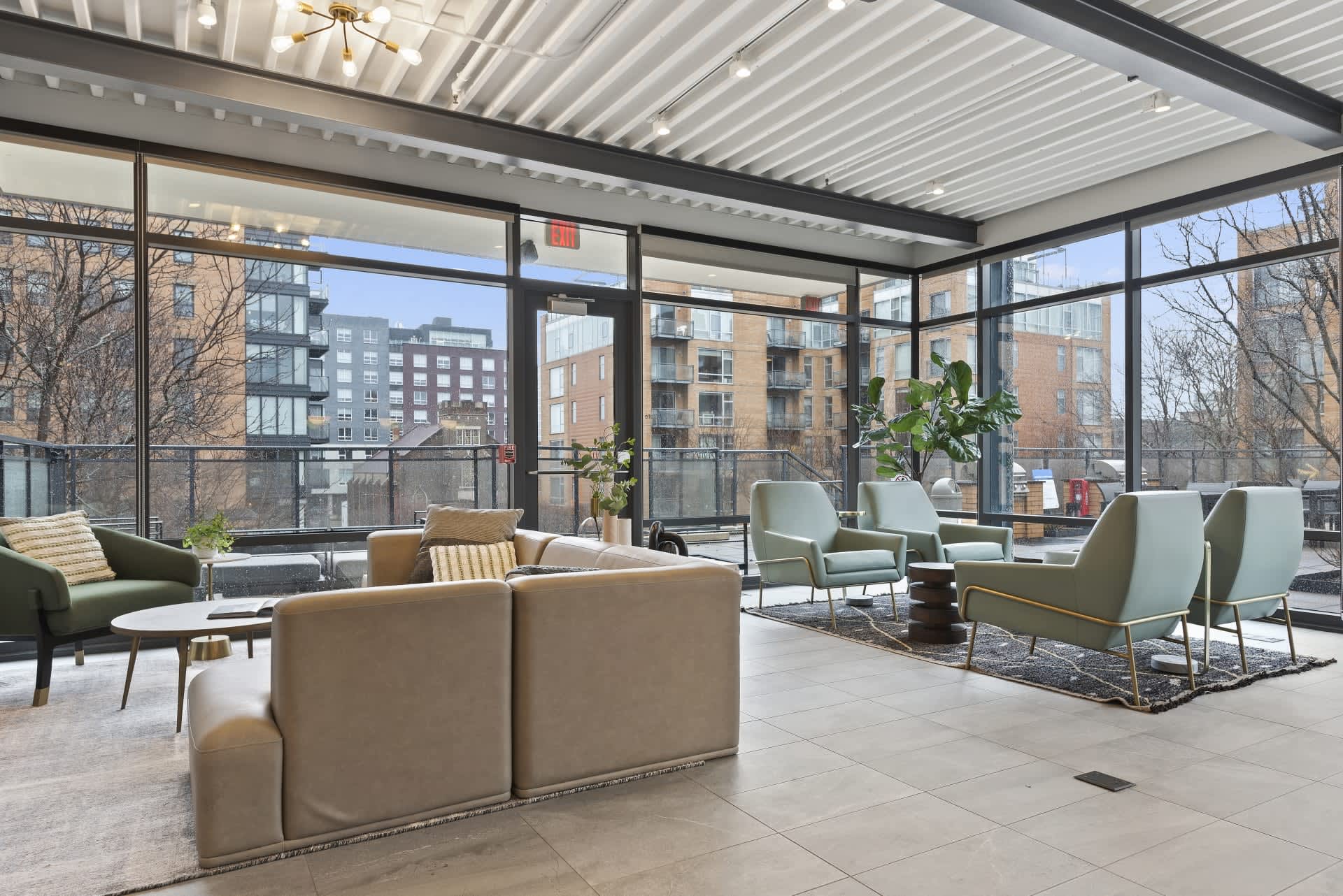 Spacious lounge with beige sectional sofa, mint green armchairs, potted plants, and expansive windows overlooking Evanston buildings.