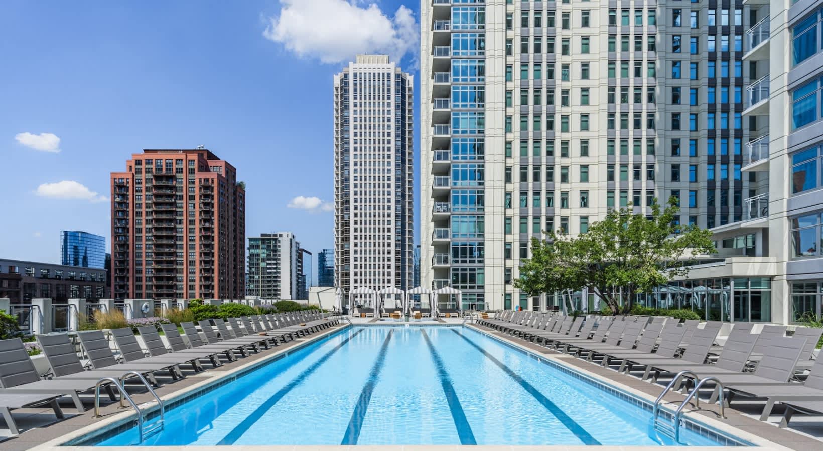 Rooftop lap pool with lane markings, gray lounge chairs on both sides, and Chicago downtown skyline with residential towers in background.