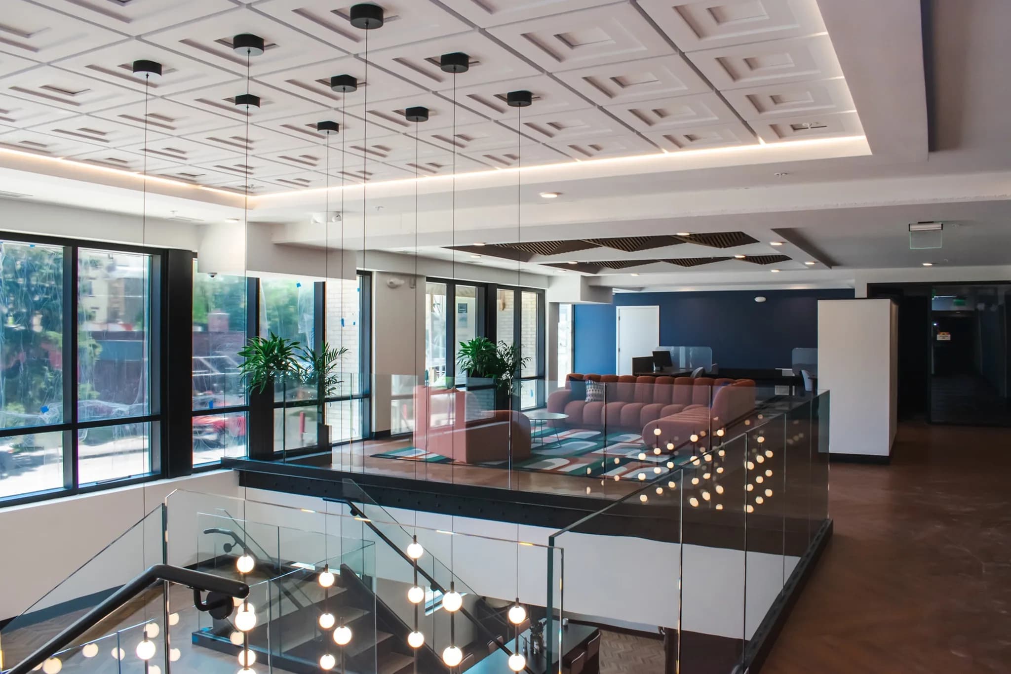 Multi-level common area with glass railings, pendant lights, brown seating, large windows, and modern ceiling design.