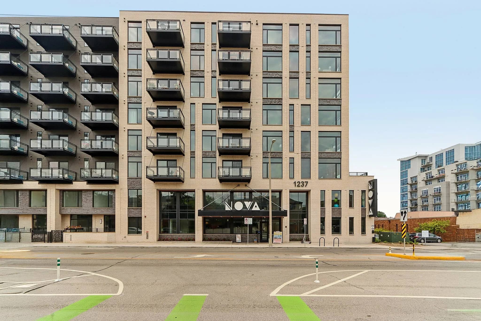 Multi-story apartment building with tan brick facade, balconies, and ground-floor Nova retail entrance on city street.