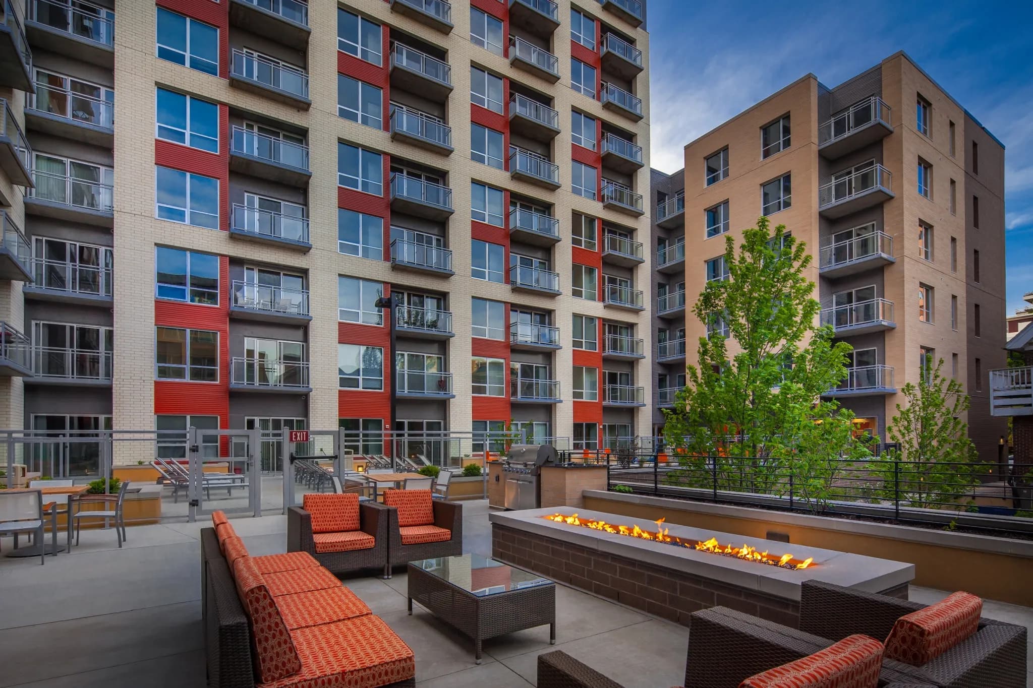 Outdoor courtyard with orange upholstered seating, linear fireplace, and multi-story brick apartment buildings with red and tan facades.