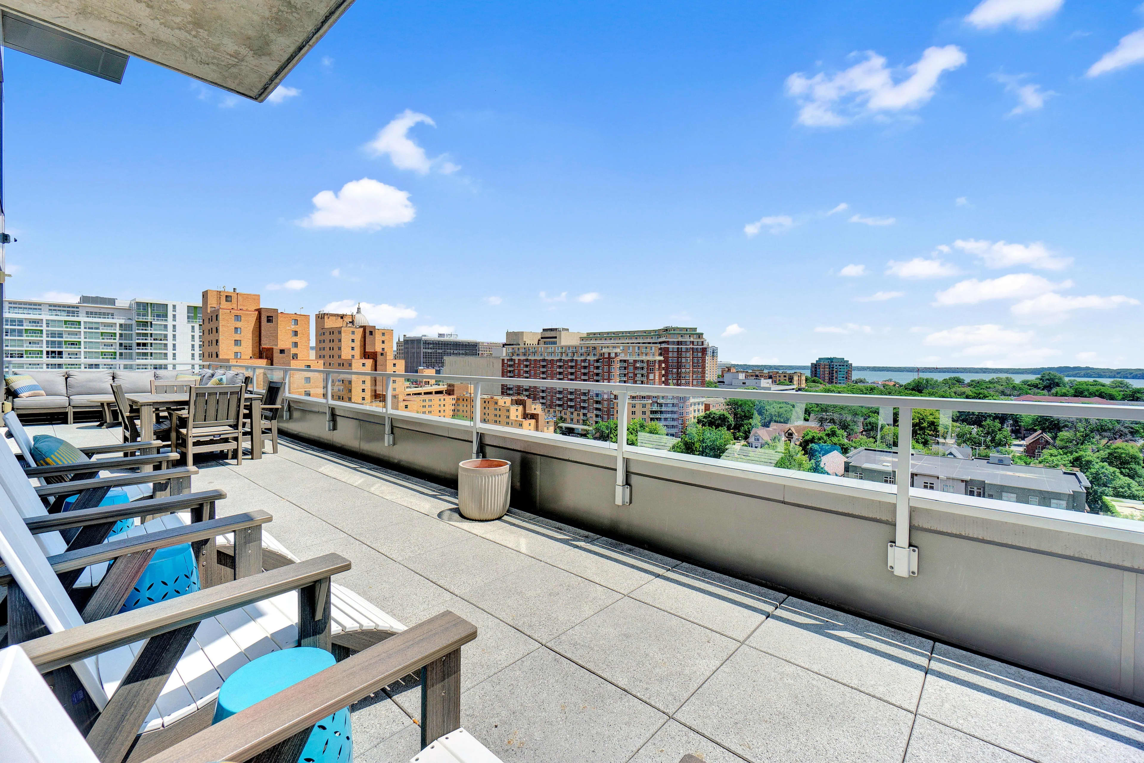 Rooftop terrace with Adirondack chairs overlooking Madison skyline, residential buildings, and distant water under blue sky.