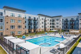 Outdoor swimming pool with lap lanes surrounded by multi-story residential buildings under clear blue sky.