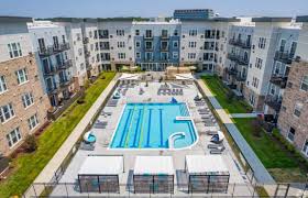 Aerial view of rectangular lap pool with lounge areas, surrounded by four-story apartment buildings and landscaped grounds.