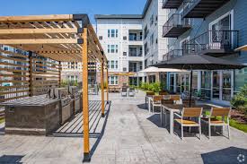Outdoor courtyard with wooden pergola, lounge seating, fire pit, and multi-story residential building in background.