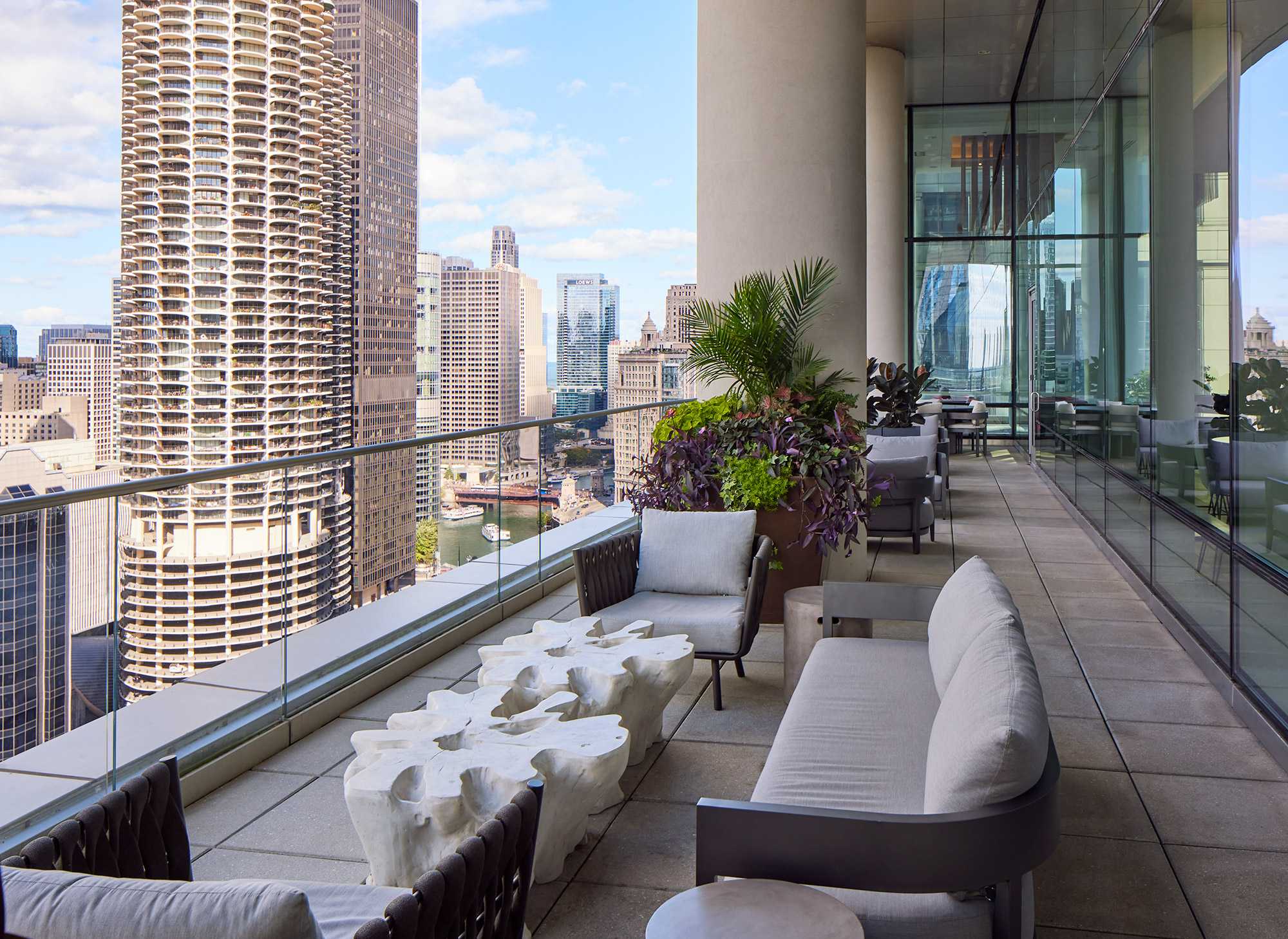 High-rise terrace with curved seating, potted plants, and expansive view of Chicago downtown skyline and Lake Michigan.