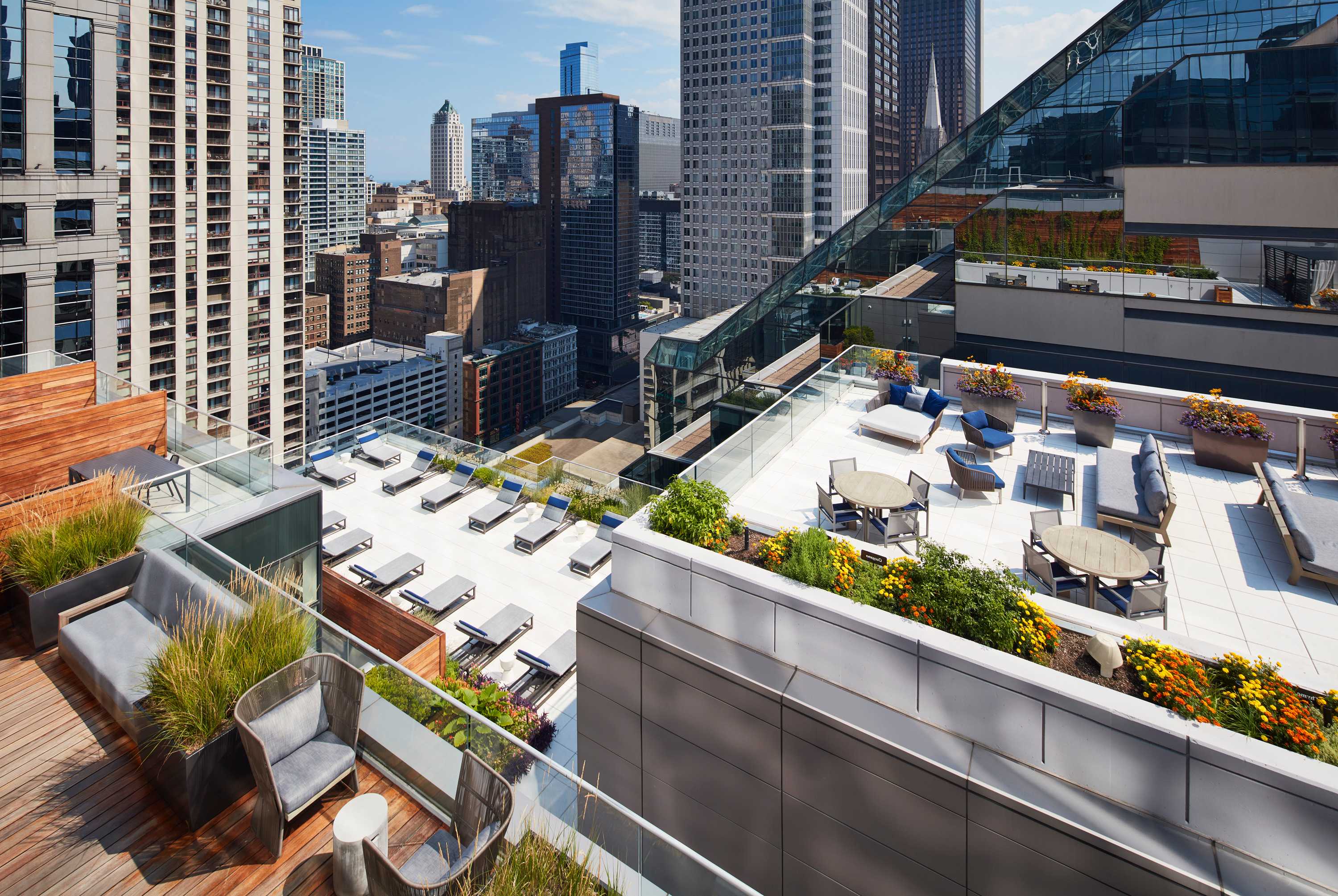 Rooftop terrace with lounge chairs, planters, and downtown Chicago skyline views surrounded by tall buildings.