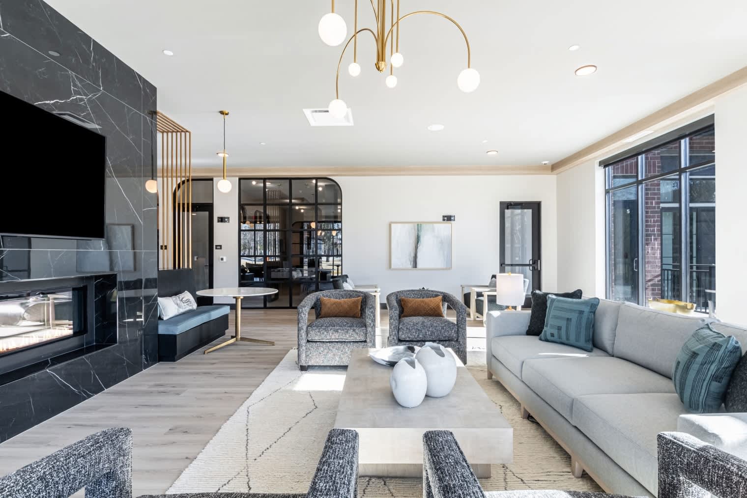 Open-concept living room with gray sofa, patterned armchairs, black marble fireplace, brass pendant lights, and wood flooring.