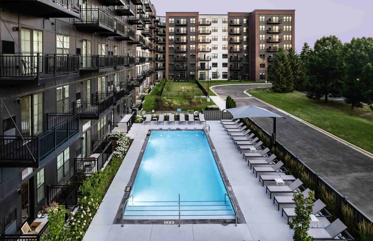 Aerial view of rectangular swimming pool with lounge chairs, surrounded by multi-story residential buildings with balconies and landscaped courtyard.