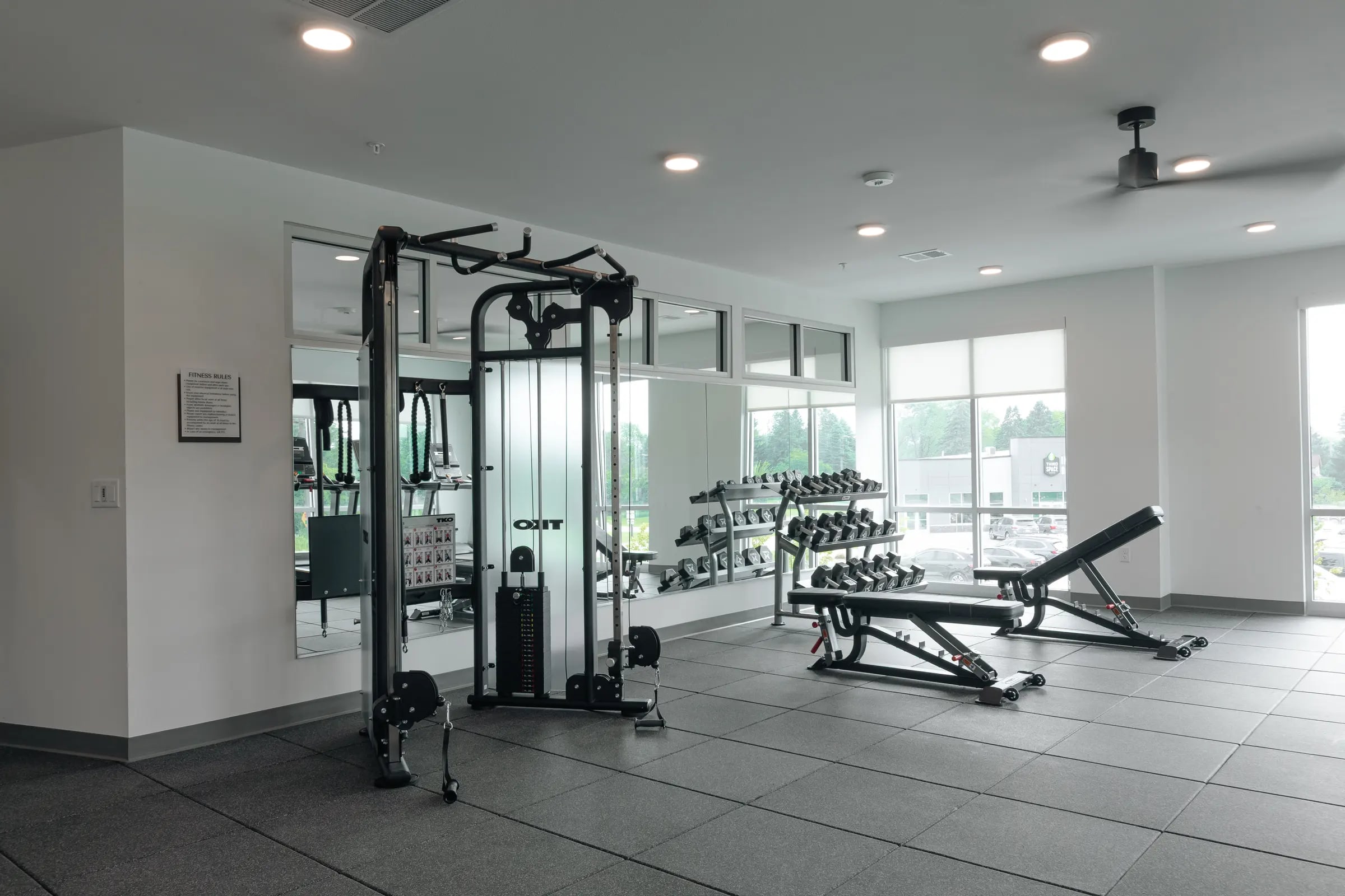 Fitness center with cable machine, dumbbell rack, weight bench, and large windows overlooking the parking area.