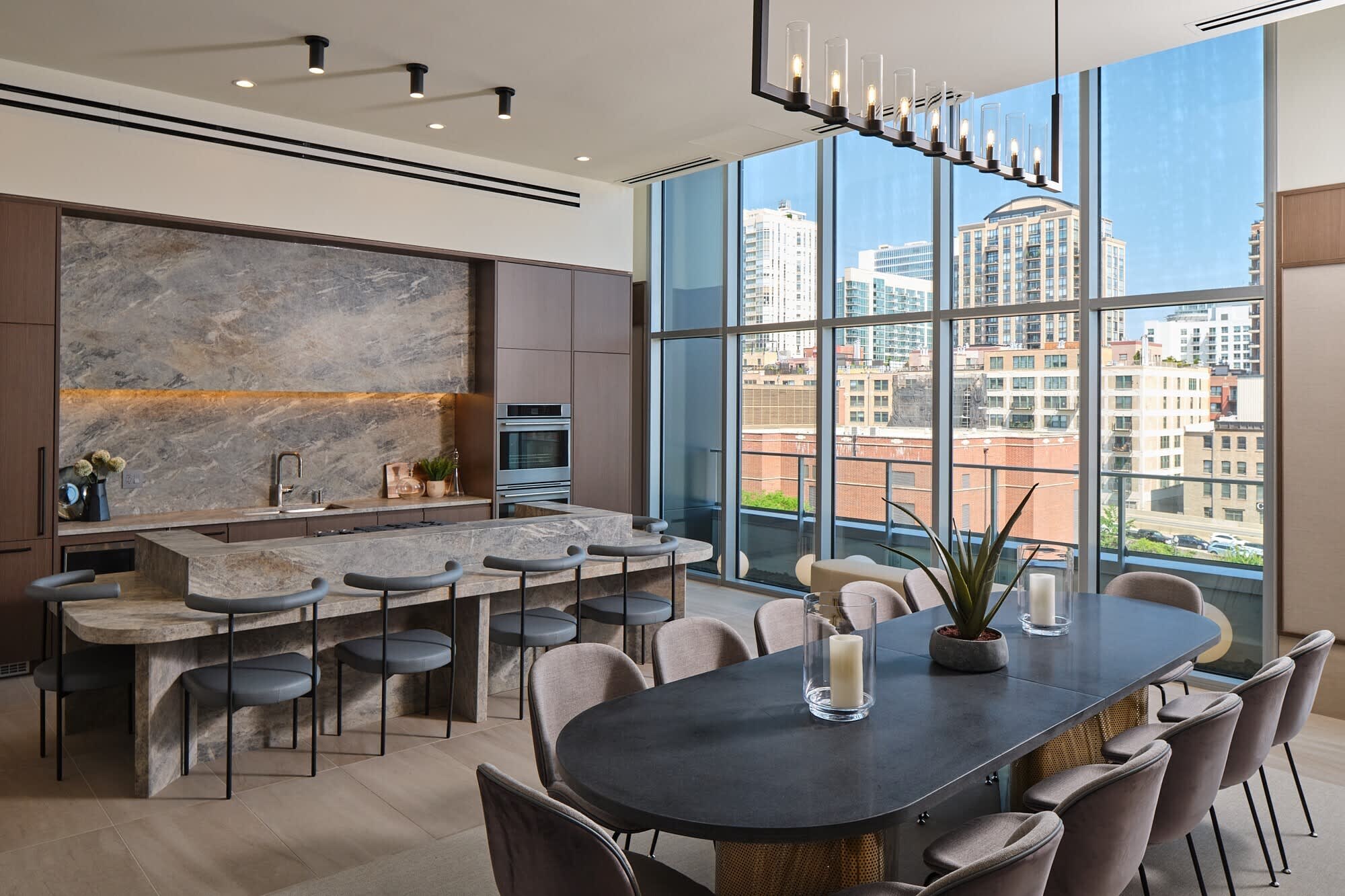 Modern kitchen and dining space with gray marble island, black dining table, and expansive windows showing downtown Chicago buildings and clear sky.