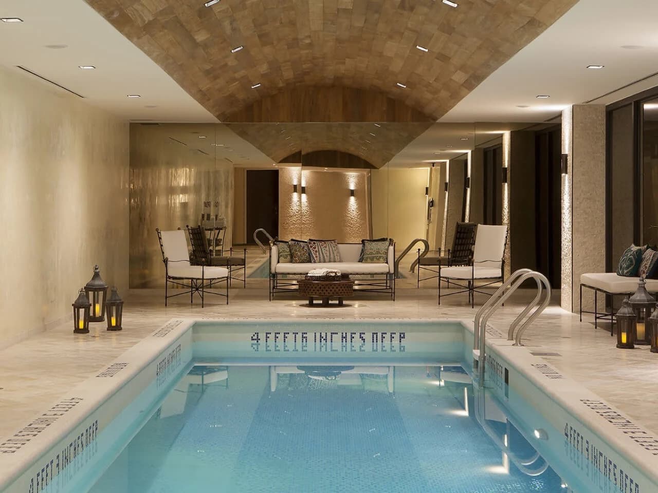 Indoor swimming pool with brick barrel vault ceiling, metal railings, lounge chairs with cushions, and recessed lighting.