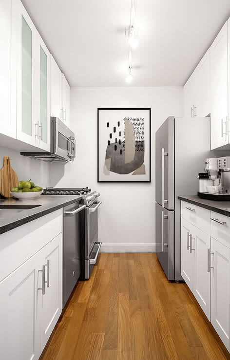 Narrow galley kitchen with white cabinets, black countertops, stainless steel appliances, and wood flooring.