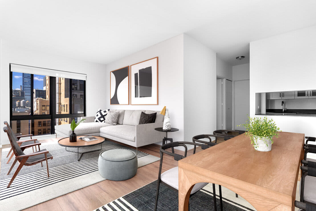Open-concept living room and dining area with white sofa, wood dining table, city views through floor-to-ceiling windows, and modern kitchen.