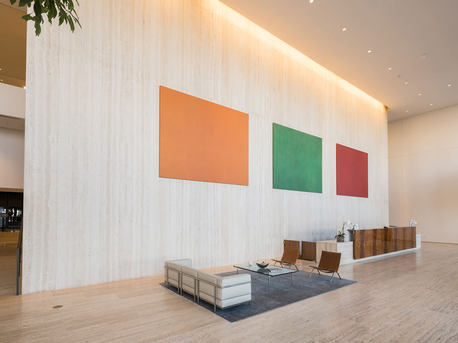 Modern lobby with light wood floors, white textured accent wall displaying three colorful rectangular artworks in orange, green, and red, mid-century modern seating, and recessed ceiling lights.