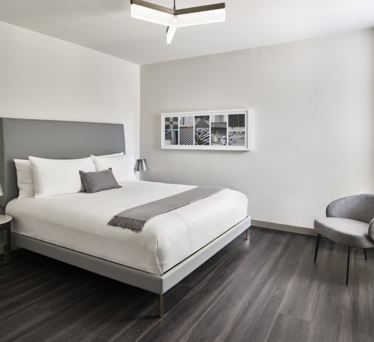 Guest bedroom with gray upholstered headboard, white bedding, dark wood flooring, and contemporary wall art.