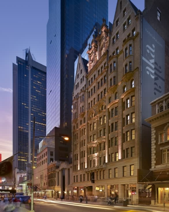 Urban street view at dusk showing historic tan and brick buildings adjacent to modern glass skyscrapers, with ground-floor retail and pedestrians.