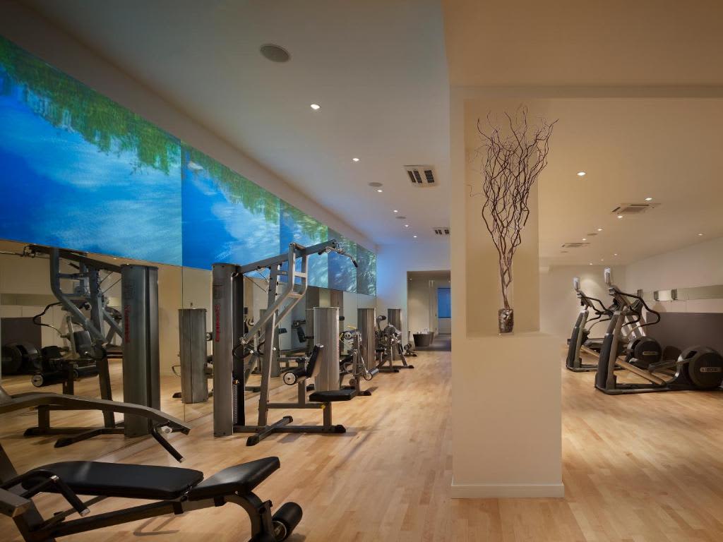 Fitness center with cardio machines, weight equipment, wooden flooring, and large blue-green nature video wall.