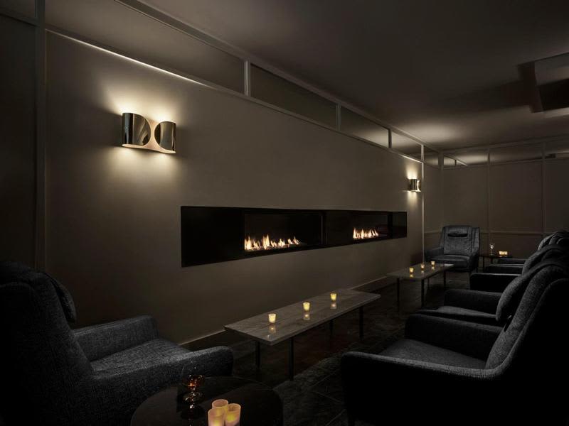 Contemporary lounge with linear gas fireplace, gray upholstered chairs, dark coffee table, and accent lighting on walls.
