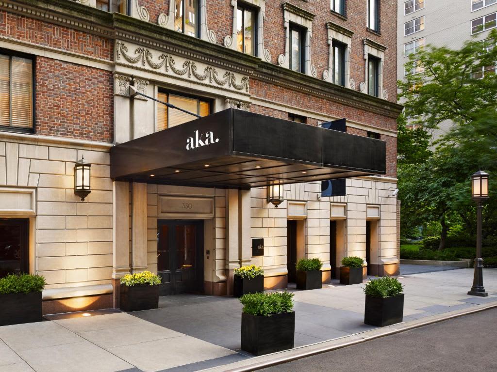 Building entrance with black awning, stone facade, ornamental cornice, planters, and ivy-covered walls.