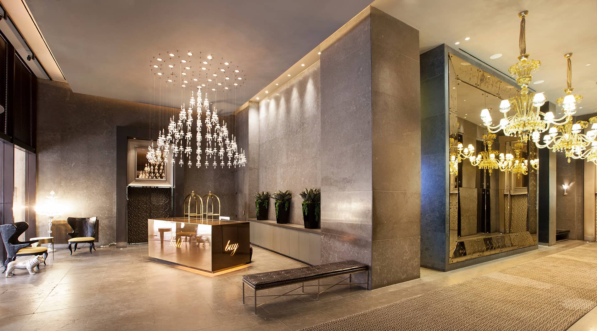 Modern lobby with crystal chandeliers, gray stone walls, concierge desk, and brass-accented fixtures.