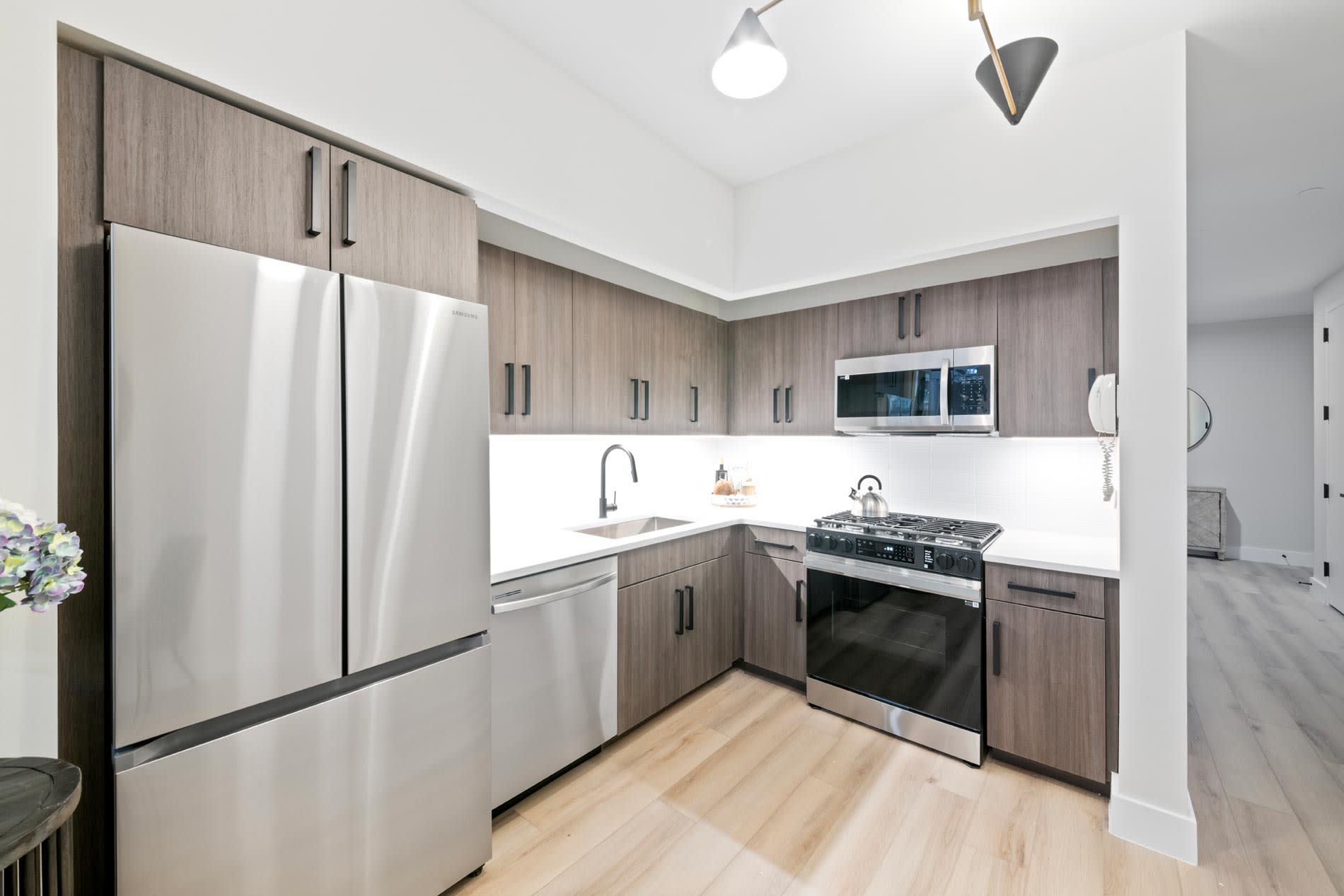 Contemporary kitchen with stainless steel refrigerator, gas range, white countertops, and wood cabinetry with pendant lighting.