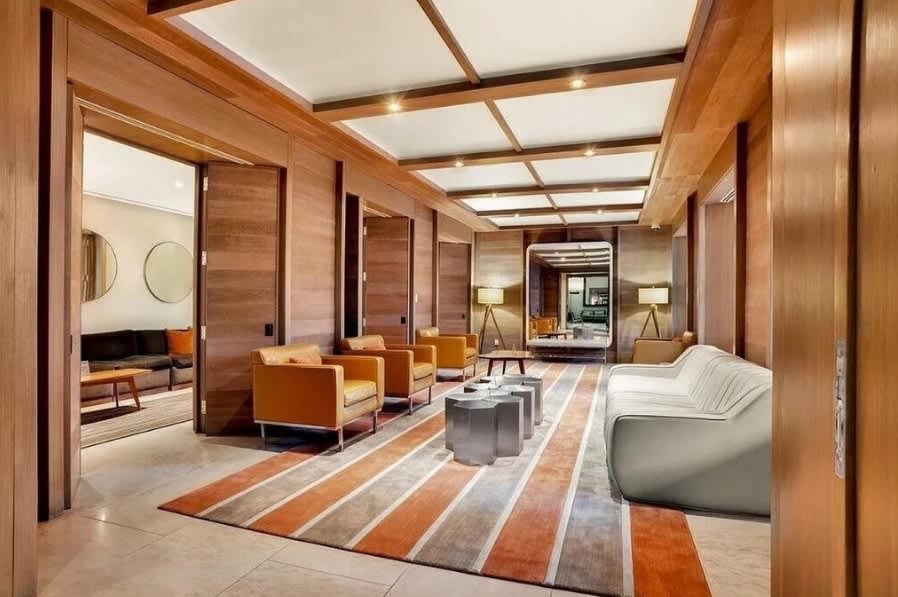 Modern lounge with wood-paneled walls, recessed ceiling lights, orange and gray striped area rug, mid-century chairs, and gray sectional sofa.