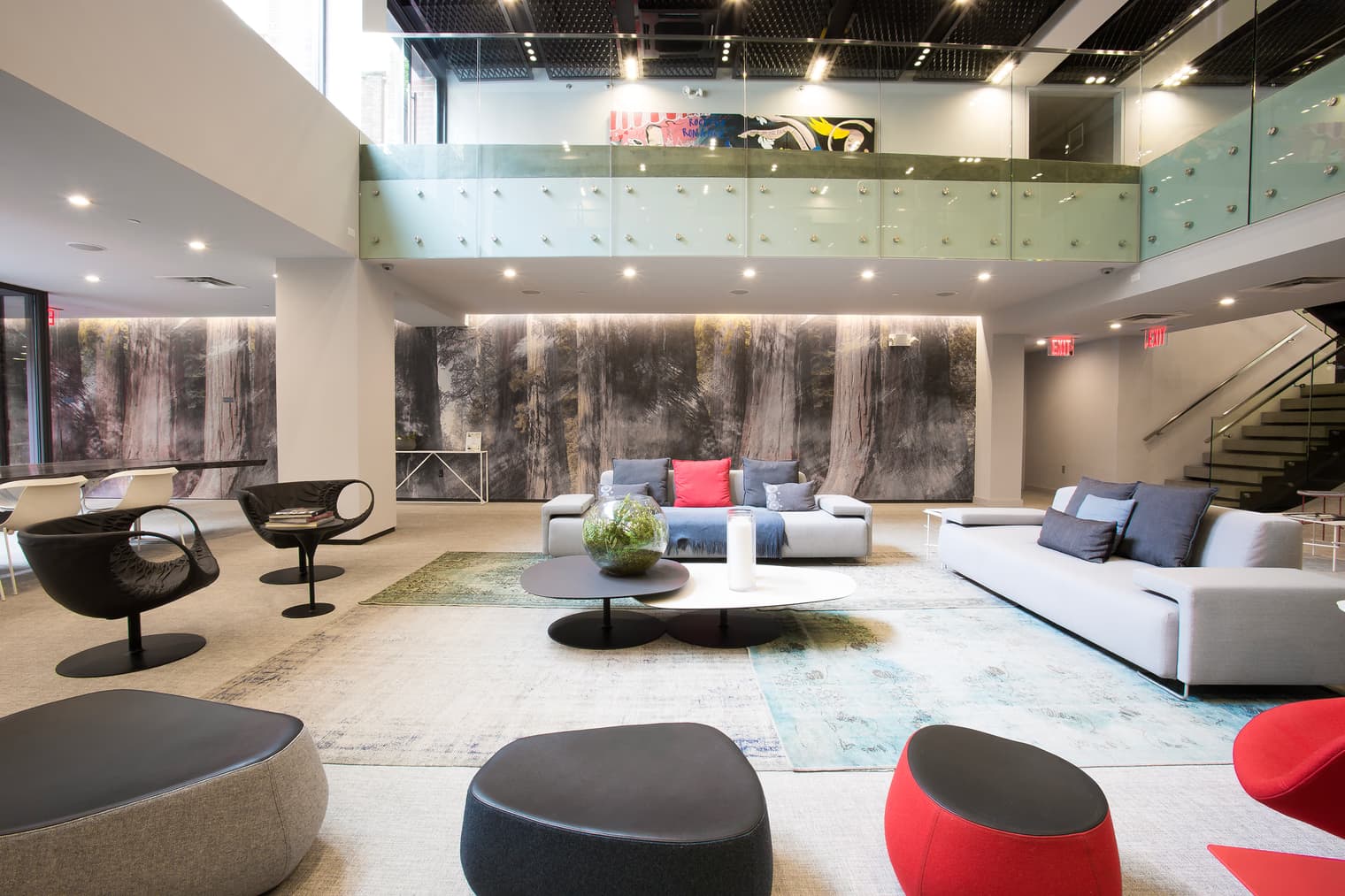 Multi-level lounge with white sofas, round ottomans, forest-wall mural, and mezzanine overlooking seating areas.