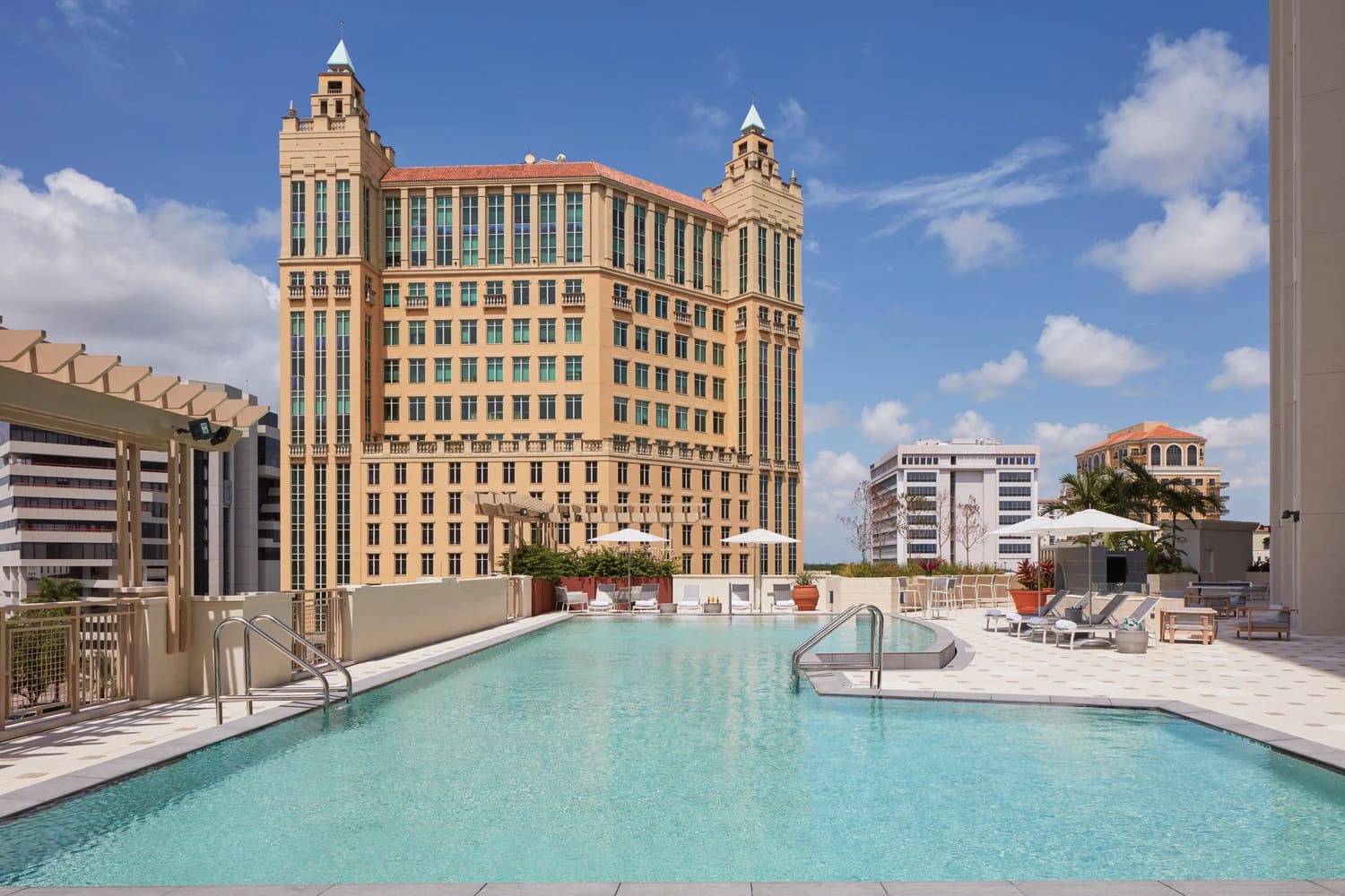Rooftop swimming pool with turquoise water, lounge chairs, and surrounding historic yellow building with twin spires in Coral Gables.