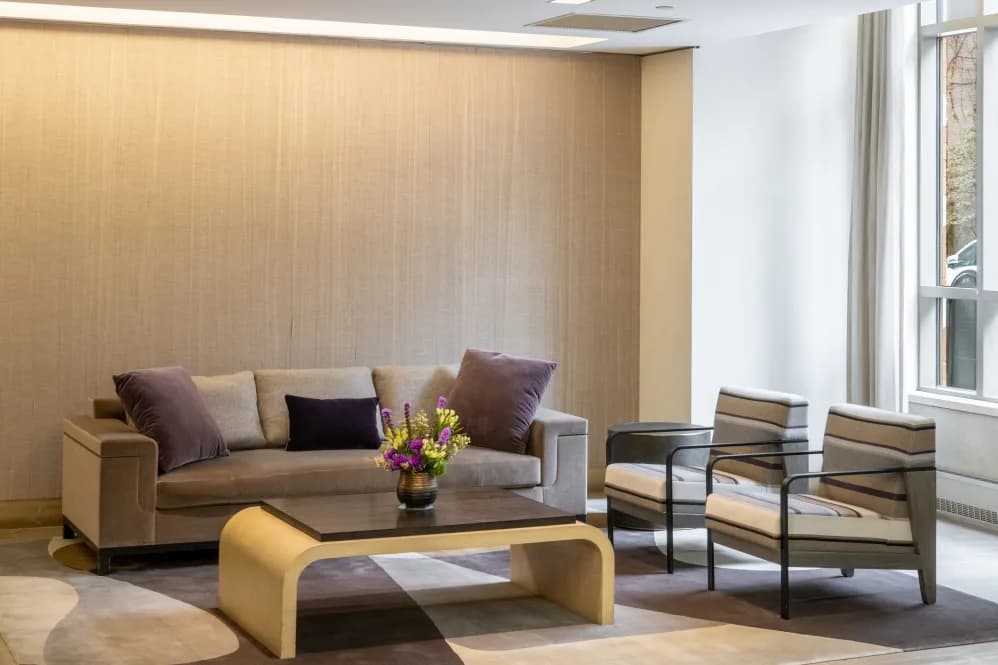 Modern living room with beige sofa, black and yellow accent chairs, dark coffee table, and tall windows with sheer curtains.