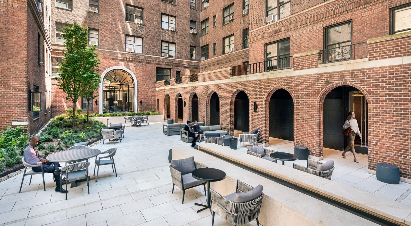 Brick courtyard with modern seating areas, arched architectural alcoves, and green landscaping in a residential building.