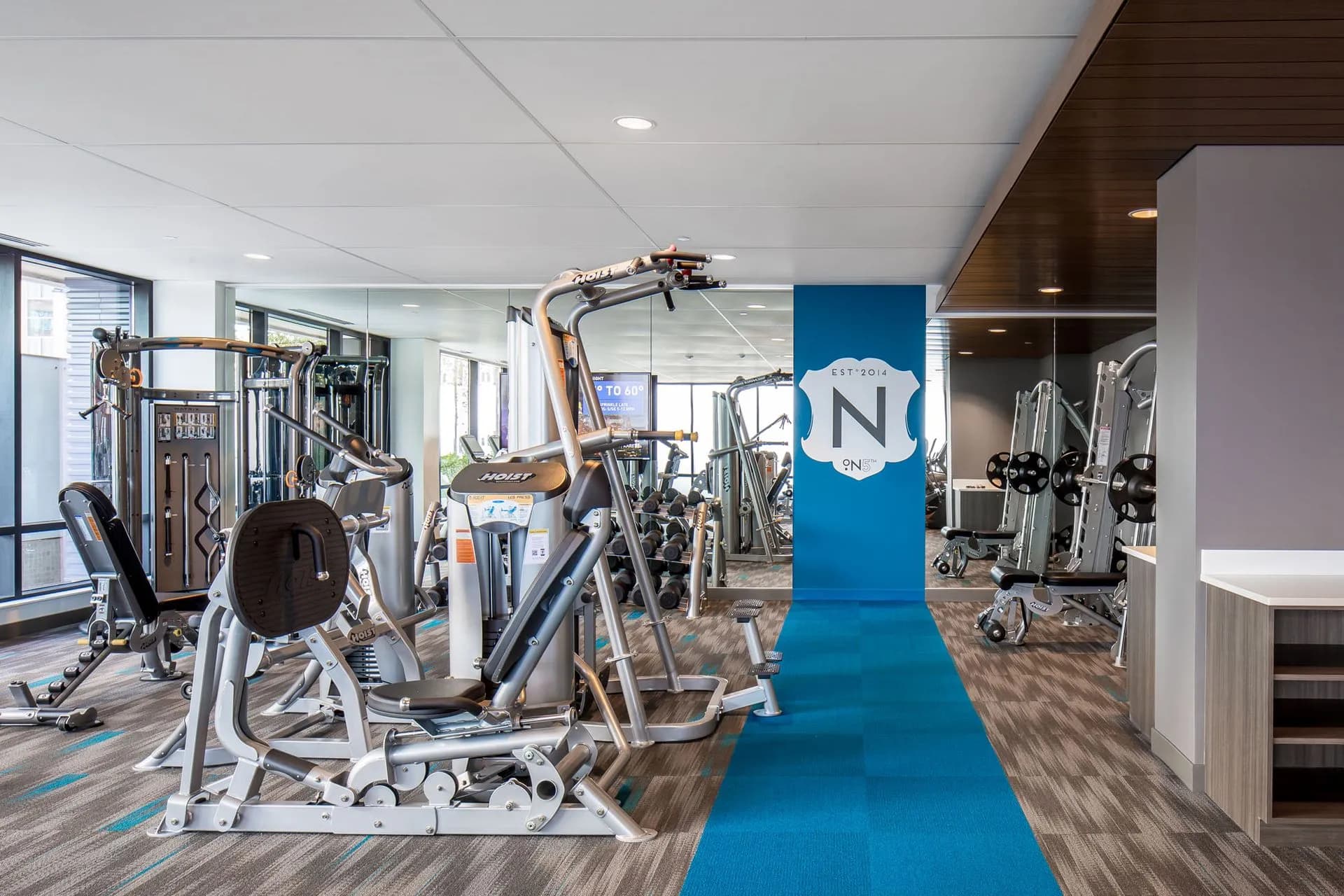 Fitness center with cardio machines, weight equipment, and blue accent flooring leading to additional workout areas.