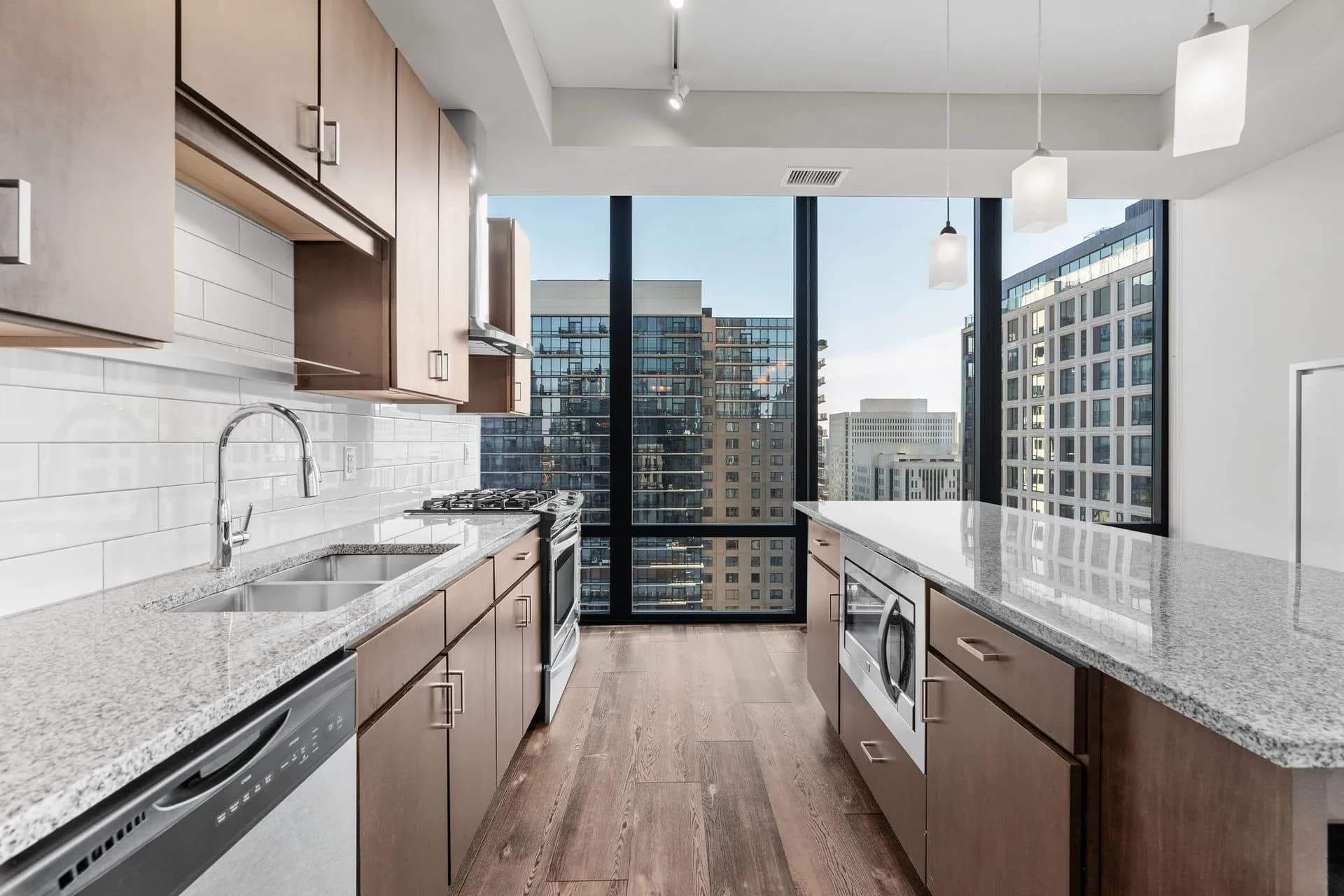 Modern galley kitchen with light wood cabinetry, granite countertops, stainless steel appliances, white subway tile backsplash, and expansive windows with downtown Minneapolis views.