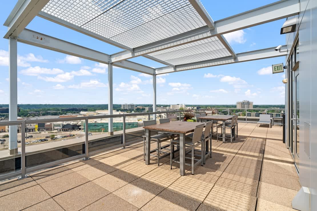 Rooftop terrace with metal pergola, dining table and chairs, expansive city skyline views, and clear blue sky.
