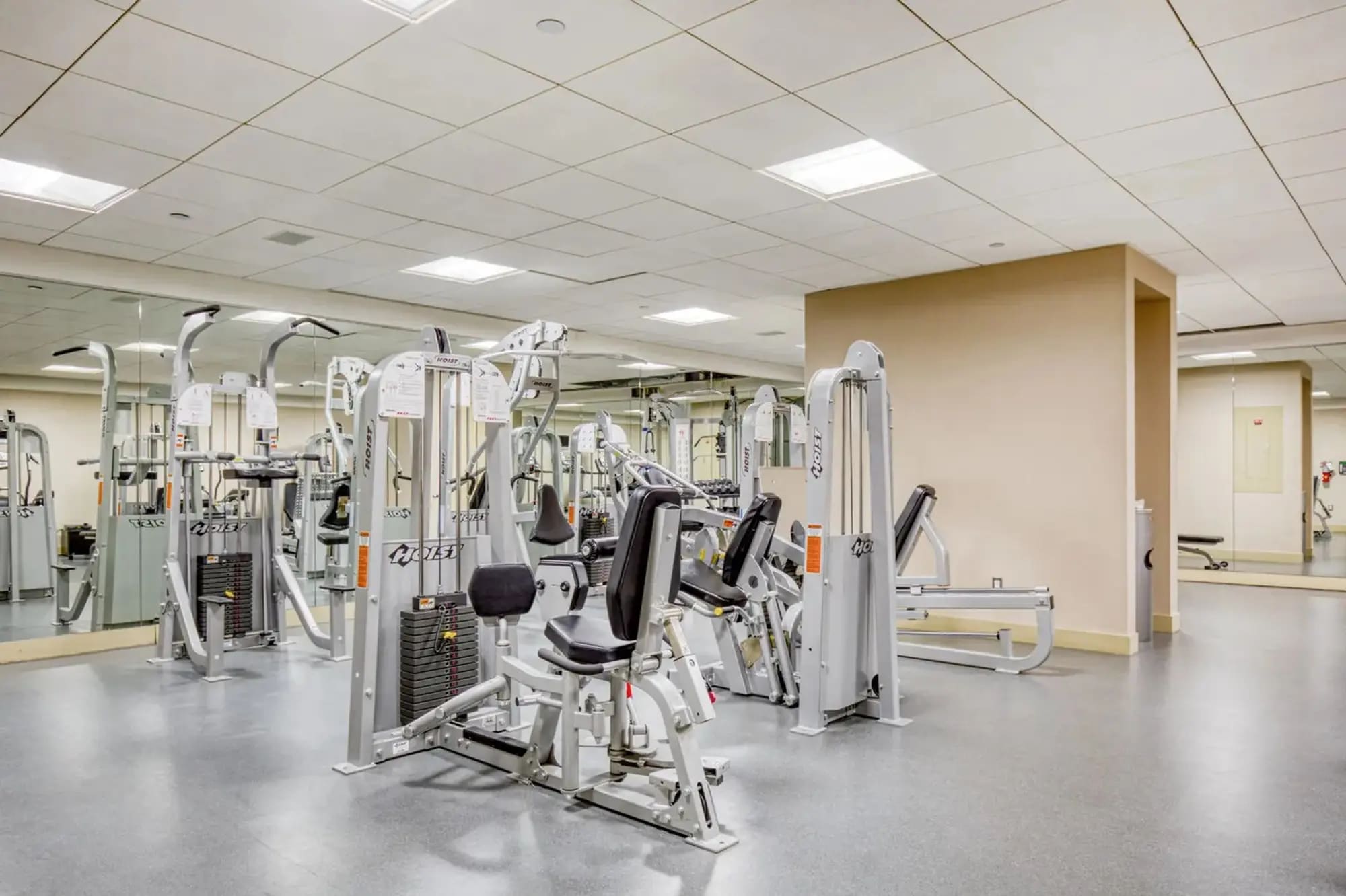Fitness center with multiple white and black exercise machines, polished concrete floor, and recessed ceiling lights.