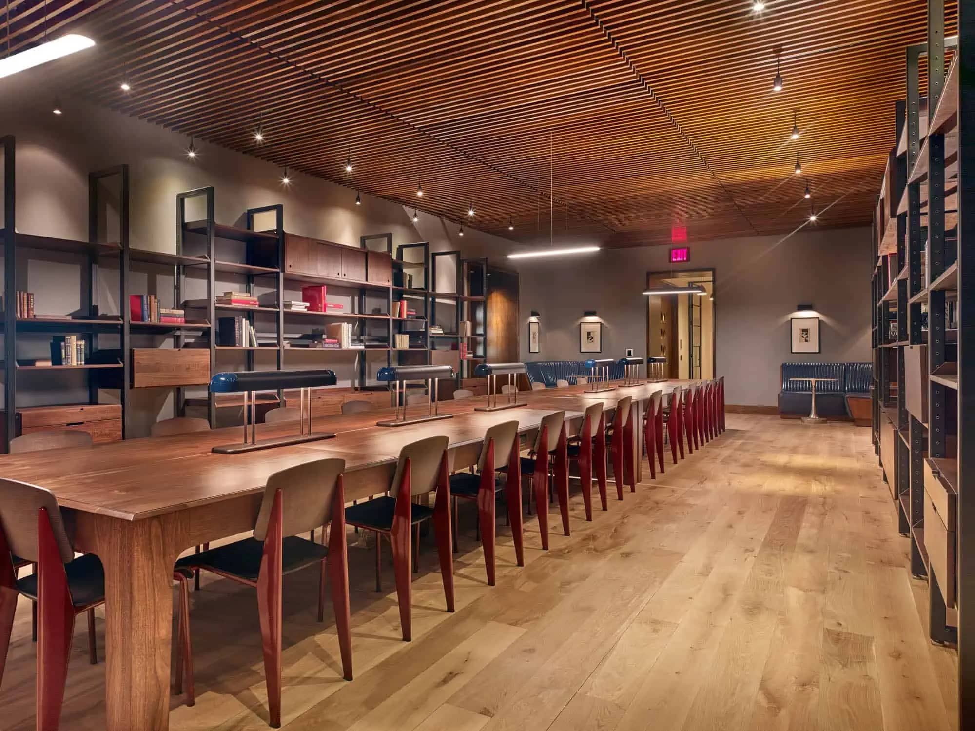 Common room with long wooden dining table, red chairs, built-in shelving, wood ceiling, and hardwood floors.