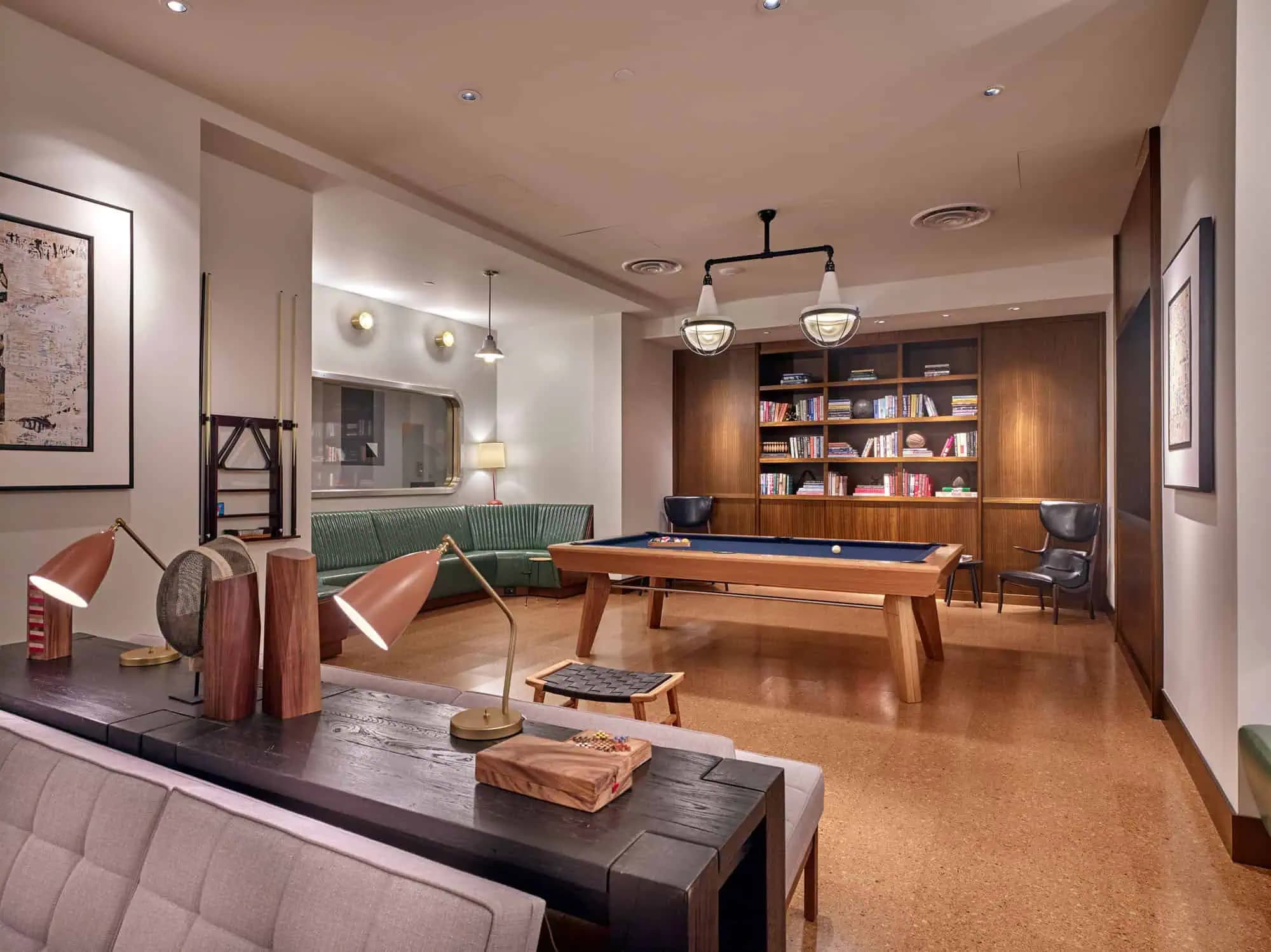 Recreation room with wood billiards table, green upholstered seating, built-in bookcase, pendant lighting, and cork flooring.