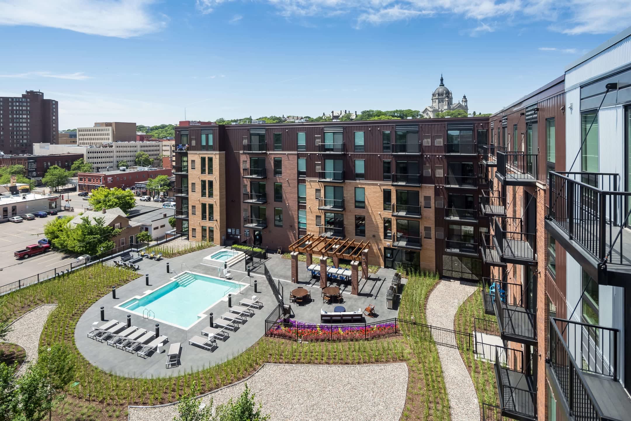 Aerial view of brick apartment complex with rectangular pool, lounge chairs, and landscaped courtyard surrounded by multi-story residential buildings.