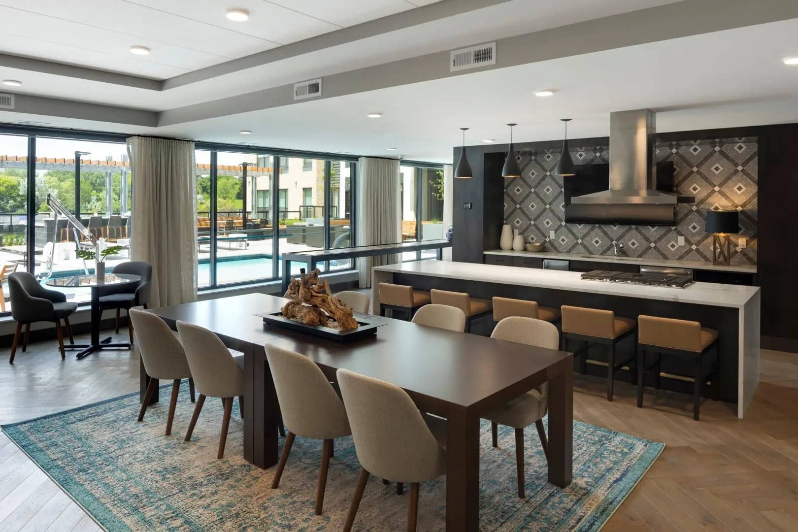 Open-concept dining room and kitchen with dark wood table, beige chairs, black kitchen island, geometric tile backsplash, and glass doors opening to pool area.