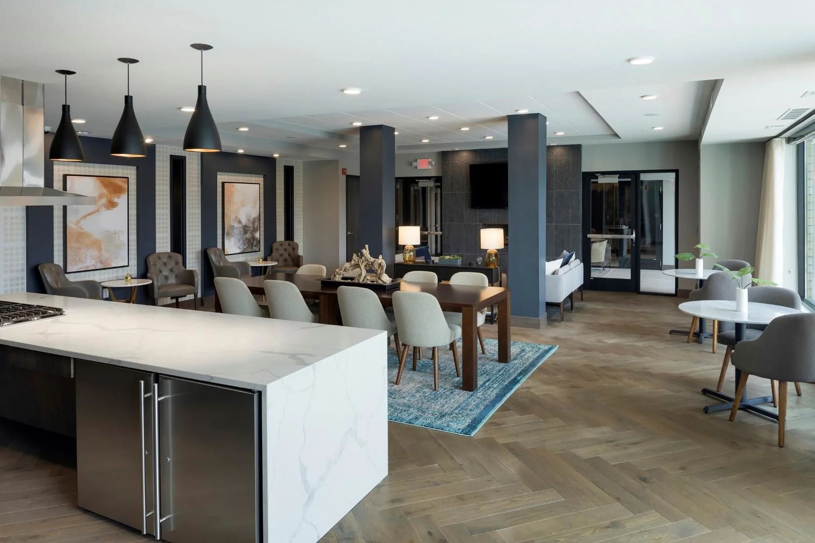 Open-concept living area with white marble kitchen island, dining table with upholstered chairs, black pendant lights, and wood flooring.