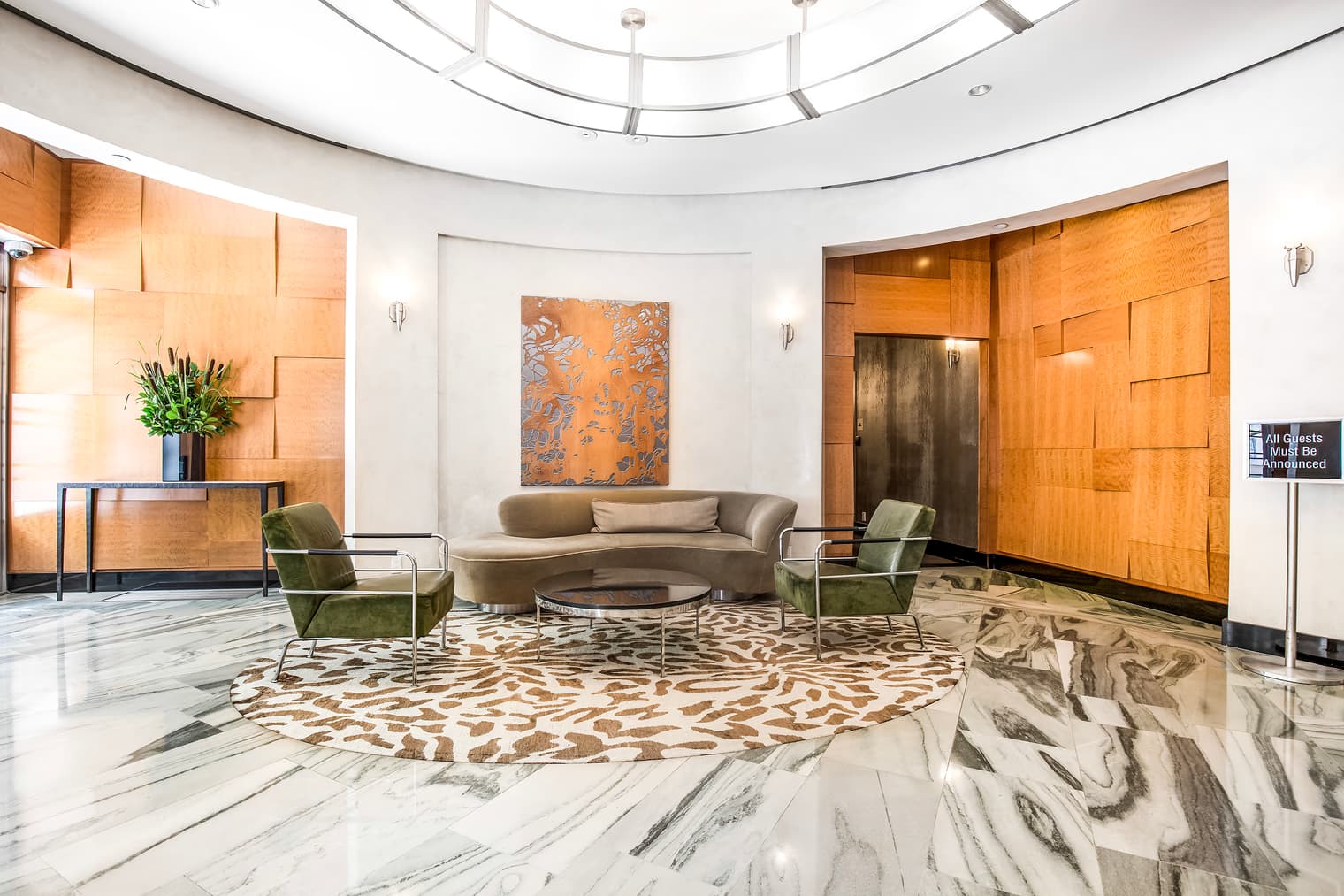 Modern lobby with curved skylight, gray sofa, green armchairs, marble floors, and orange wood-paneled walls.