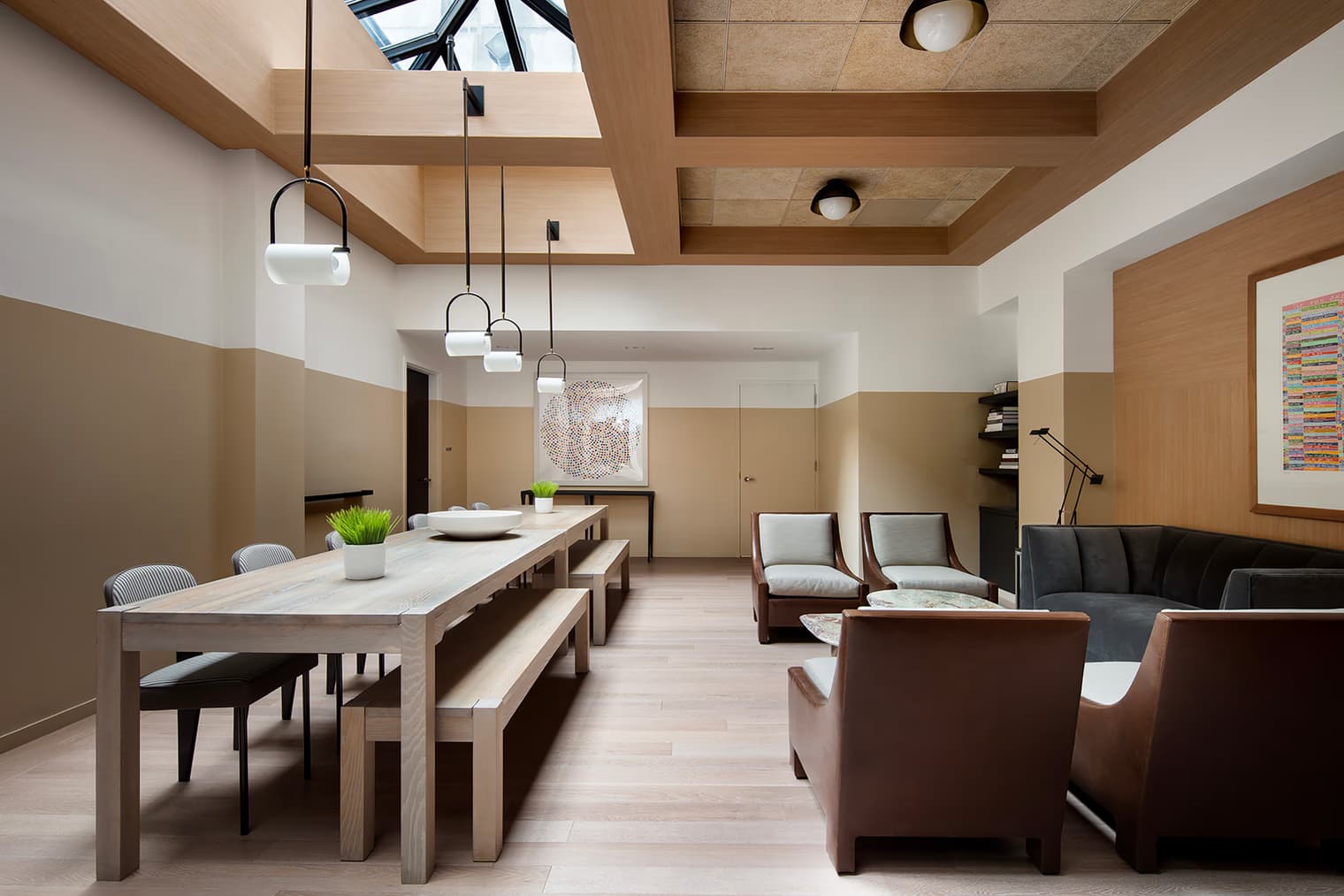 Open common area with light wood dining table, brown leather chairs, pendant lights, and skylight ceiling in neutral tones.