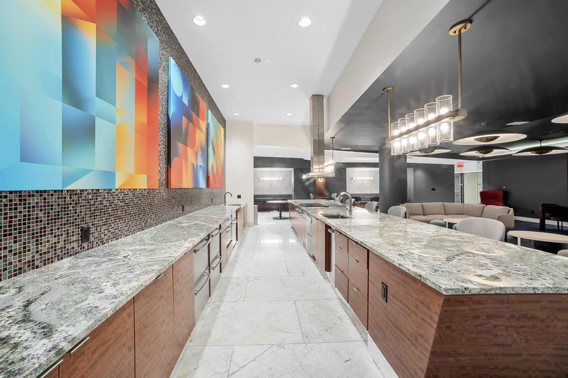 Modern kitchen with two granite-topped wooden islands, small-tile backsplash, and vibrant blue-orange-yellow geometric wall art.