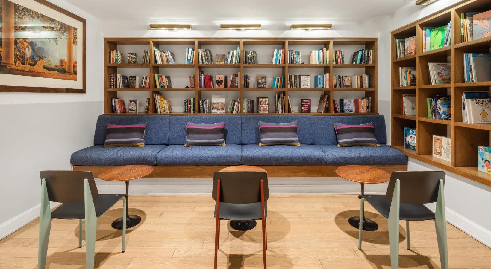 Common room with blue sofa against wall of wooden bookshelves, modern chairs around small tables, and wood flooring.