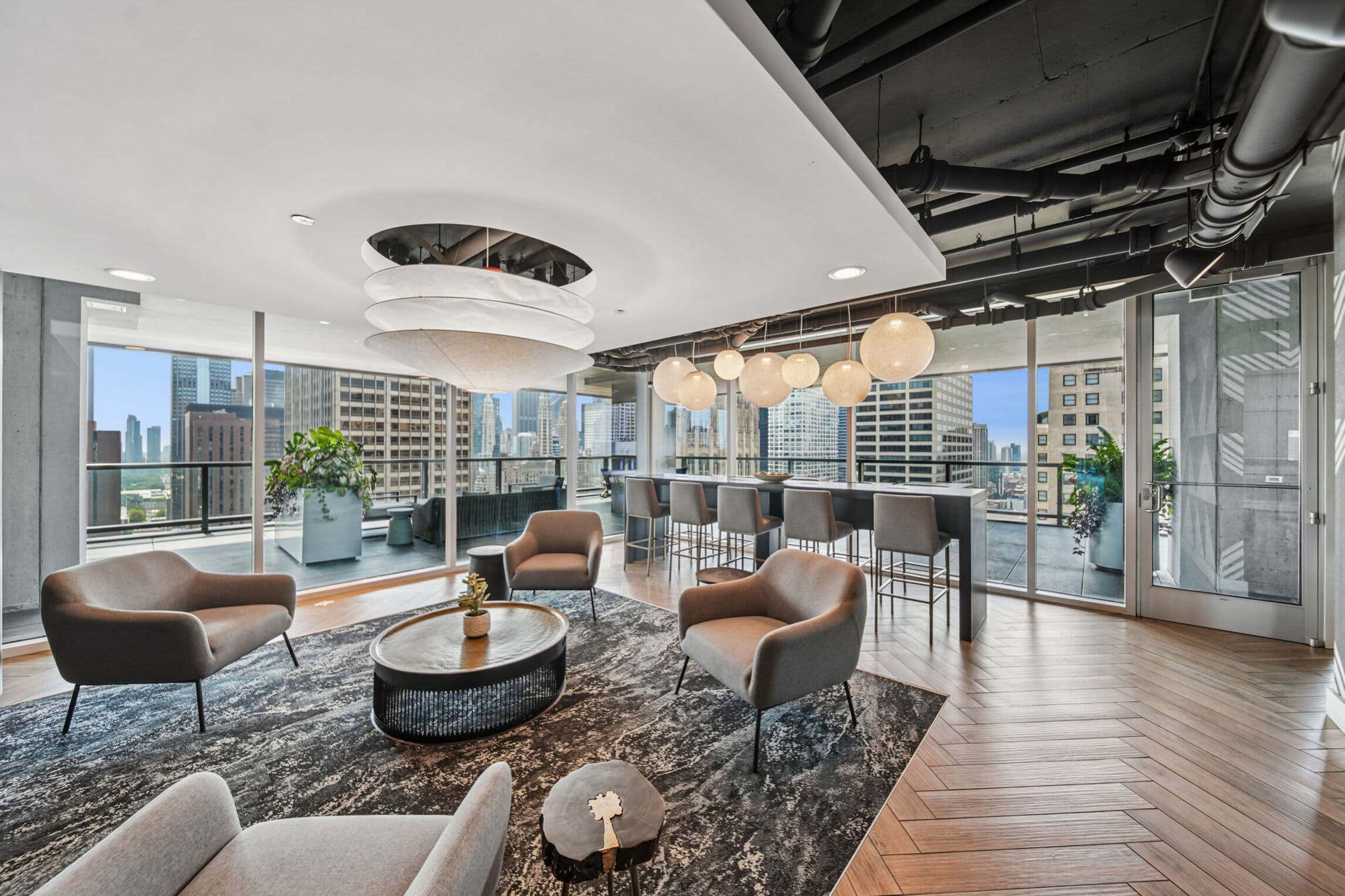 High-rise lounge with brown leather chairs, round coffee table, pendant lights, and expansive windows showing Chicago skyline and downtown buildings.
