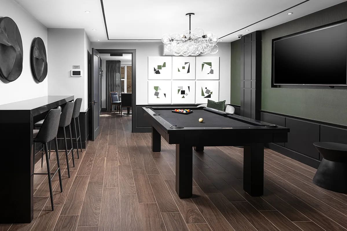 Recreation room with black pool table, bar counter with seating, wall art, crystal chandelier, and flat-screen TV.
