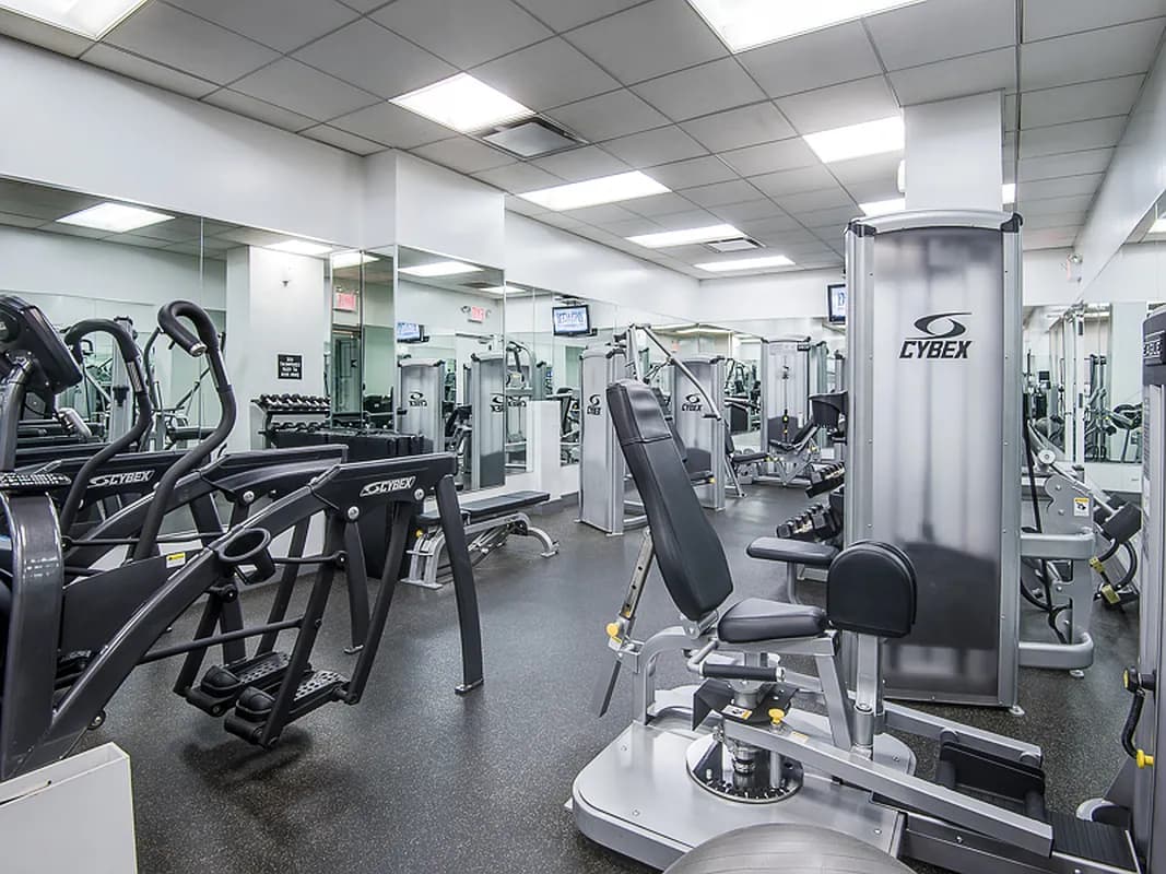Fitness center with Cybex exercise equipment including ellipticals, weight machines, and mirrors under bright ceiling lights.